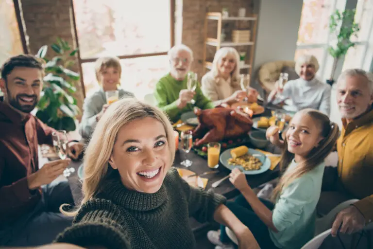 Events-Arizona photo of big family sit feast dishes table around roasted turkey multi generation relatives making group selfies raising wine glasses juice in living room indoors